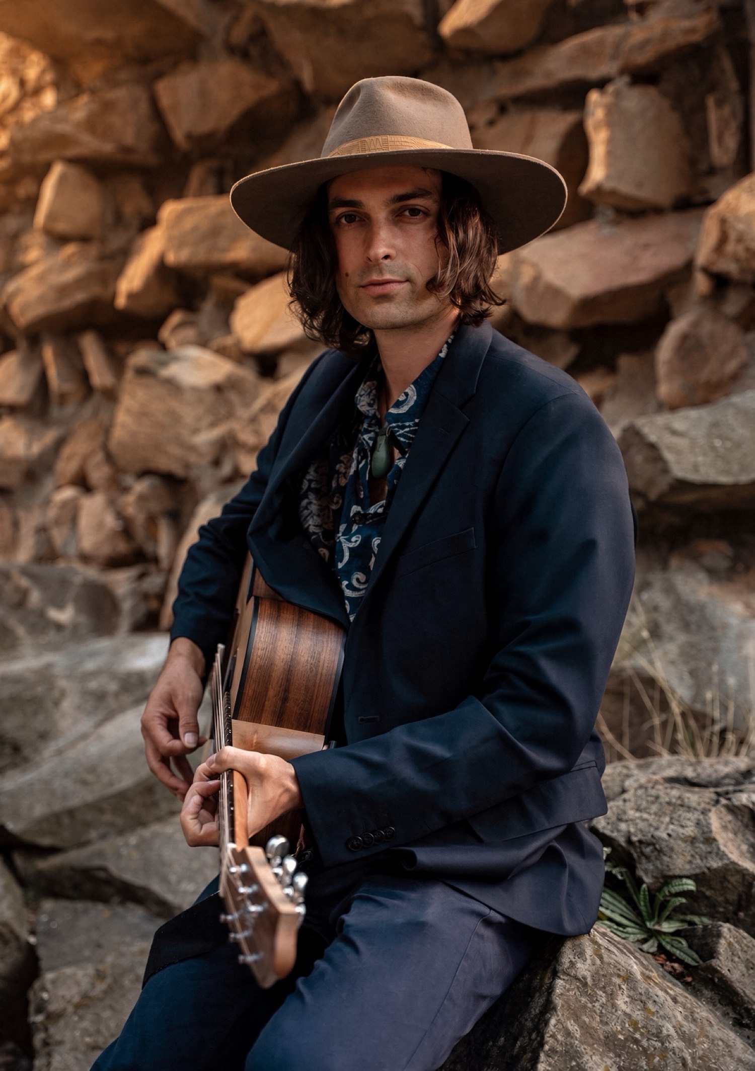 Luke Greenstone sitzt mit Gitarre auf Felsen